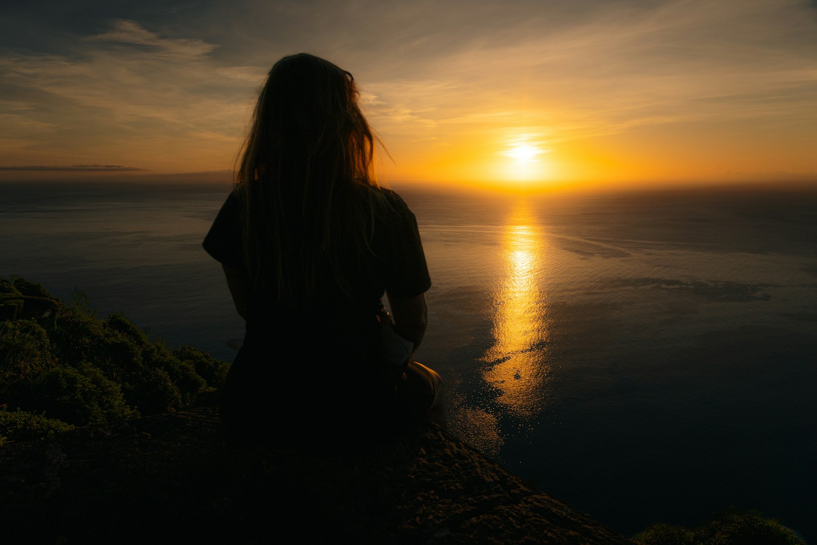 A woman sitting on a cliff watching the sunset